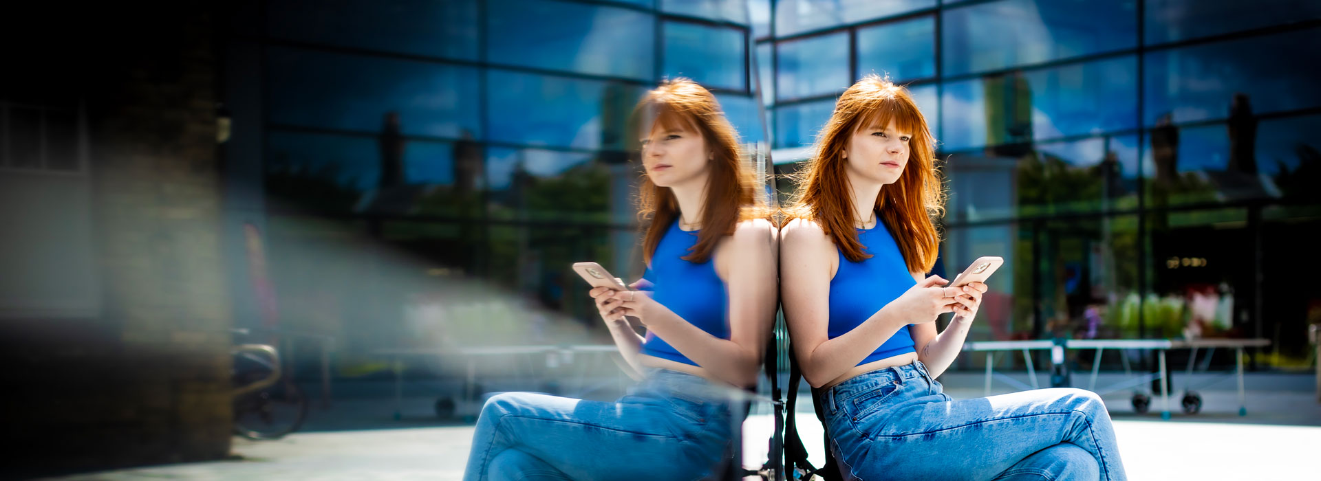 Student sitting outside on Leicester campus, whilst looking at her phone.