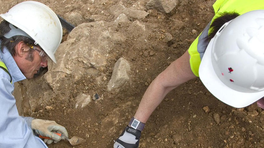 Two people in hi vis jackets and helmet, digging into the ground.