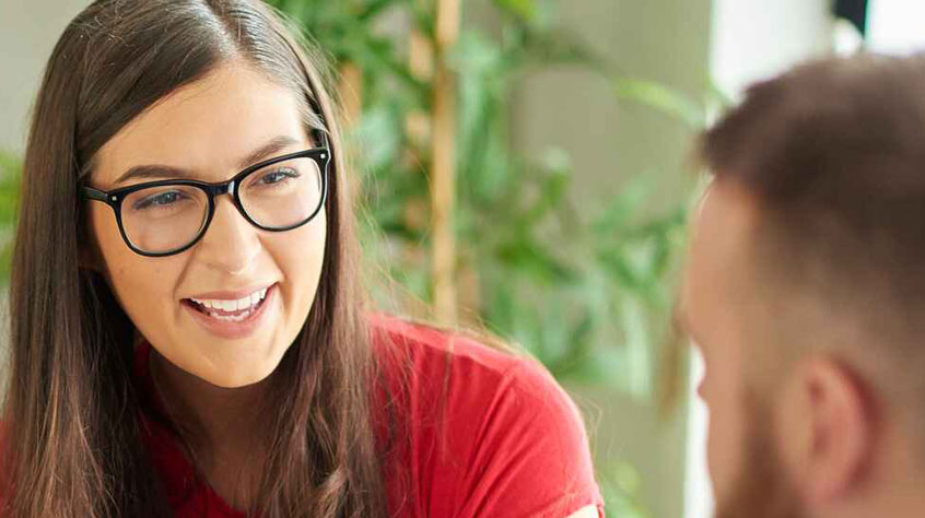A woman with glasses, in a red top laughing.