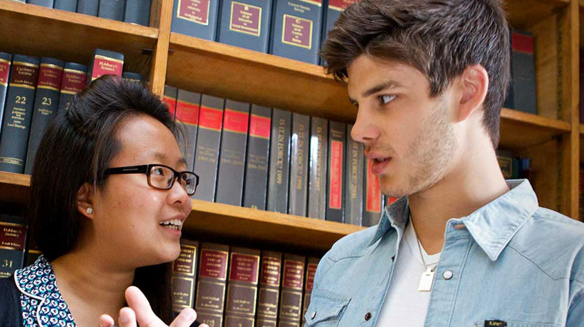 Two people talking to each other, with a backdrop of books on a shelf.