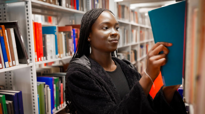 Student pulling a book down from a shelf in the library.
