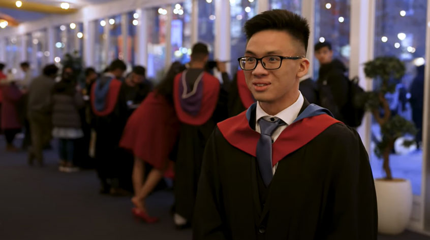 Student wearing a cap and gown and speaking to camera