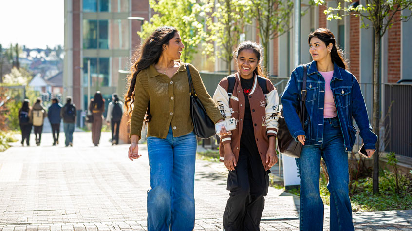 Three women walking together on a university campus. They are all smiling.