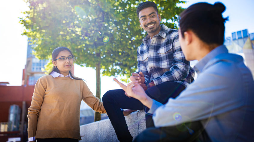 Three students sitting on campus and talking
