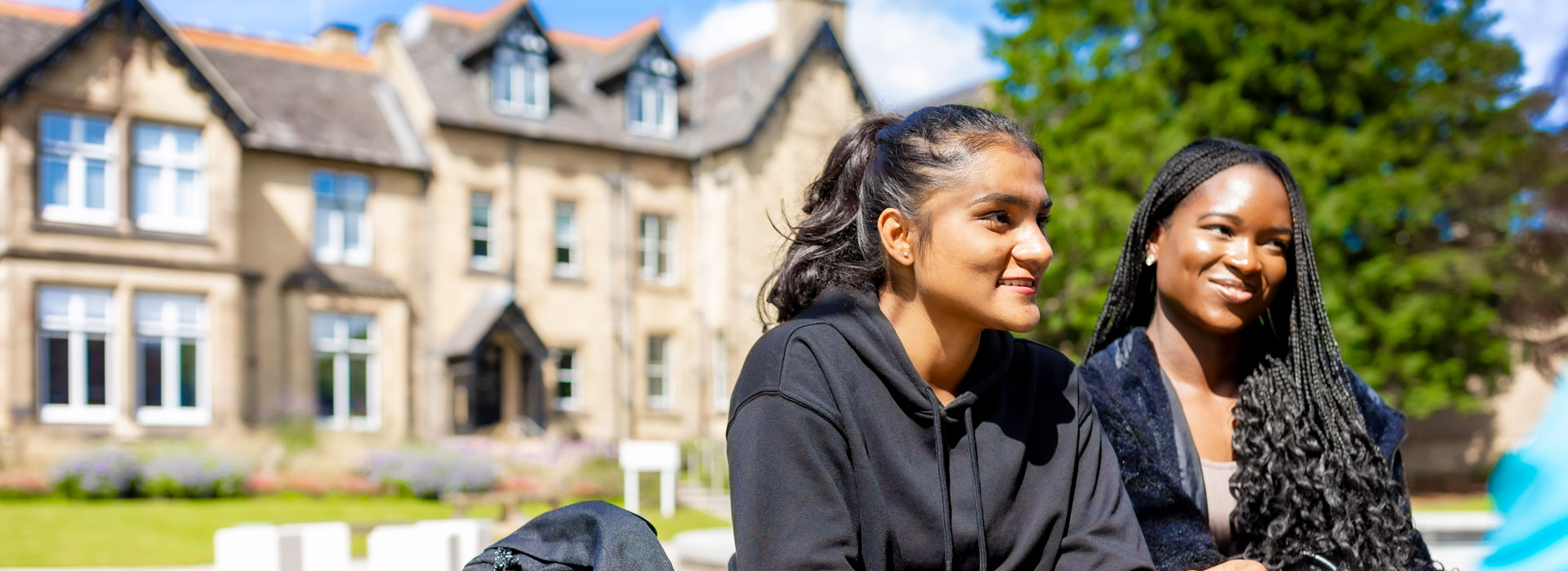 Students sitting on a bench on campus and smiling.