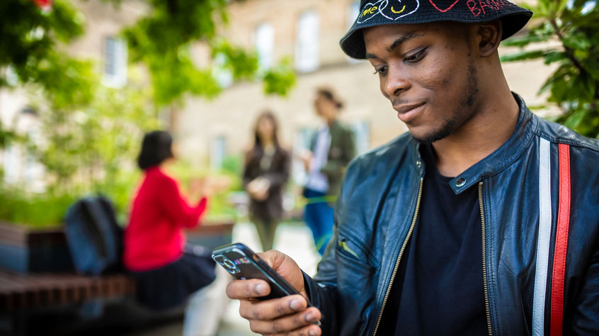 Student standing on campus and looking at his phone.