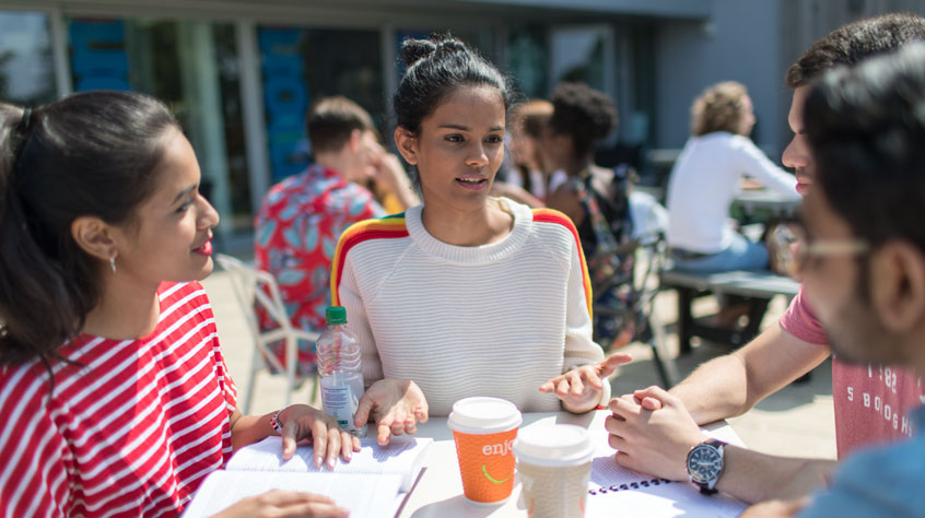 Students sitting on a table outside the Students' Union with papers and coffee cups on the table.