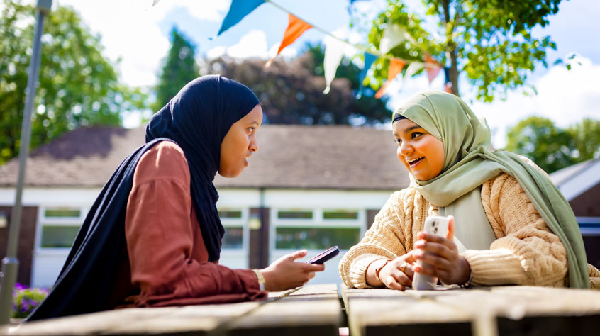 Students sitting outside on a bench looking at one of their phones.