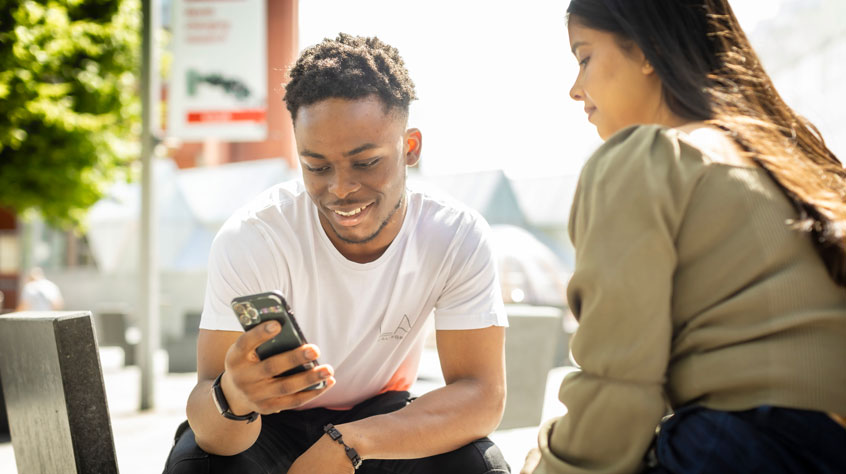 Students sitting outside on campus and looking at a phone together.