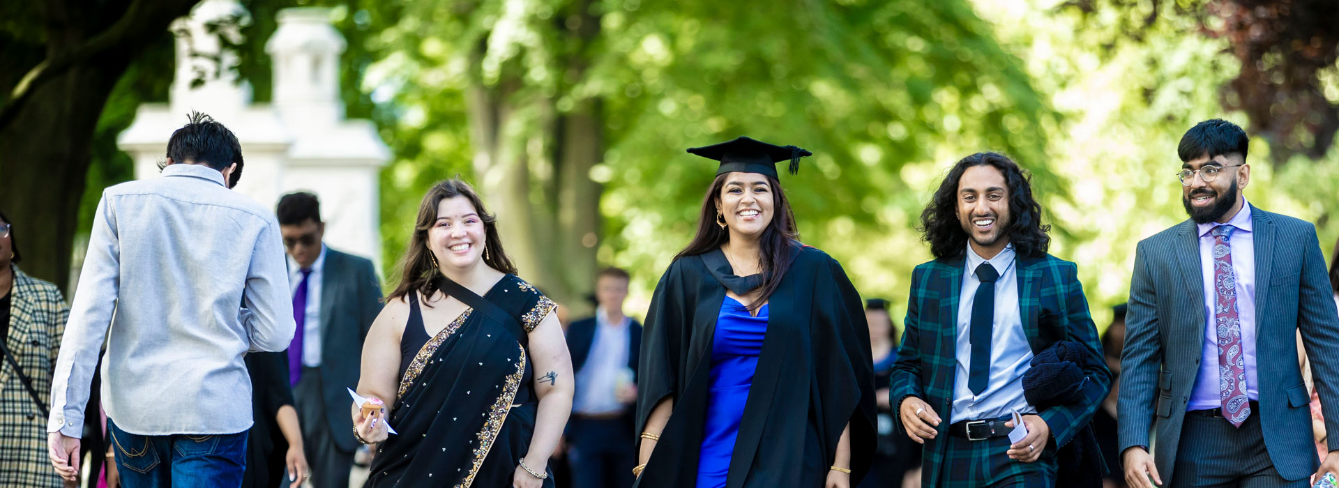 Student in cap and gown walking through a park with her family.