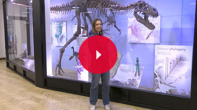 Student posing for a picture in front of 'Jane' the dinosaur on Leicester campus.