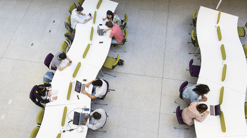 Students sitting across two long desks working on a laptop. 
