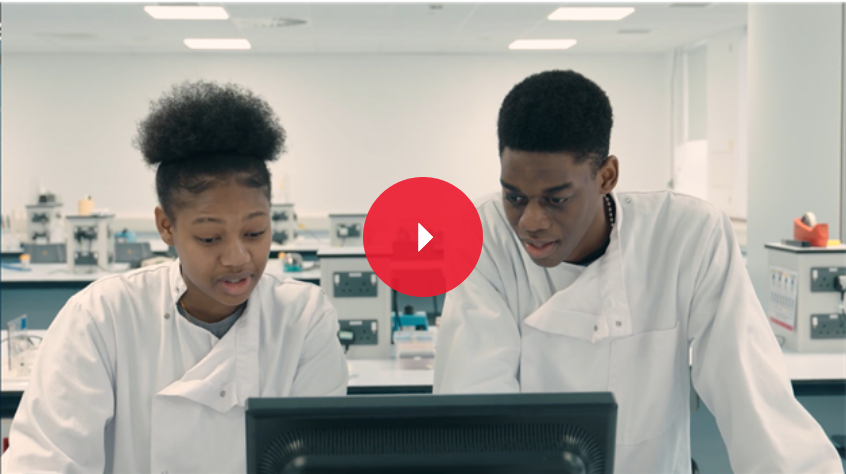 Two biological sciences students in a lab, wearing white coats and protective eye wear, looking at a screen of information