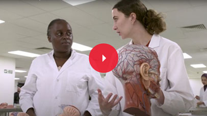 Two students in lab coats with a dissection dummy next to them.