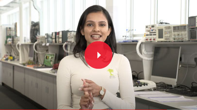Student standing in an engineering lab and smiling into the camera.
