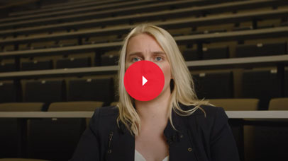 Woman with blonde hair sitting in an empty lecture theatre and talking to camera