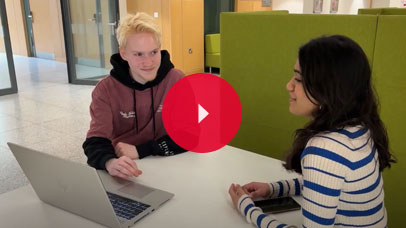 Students sitting together at a table, with a laptop between them.