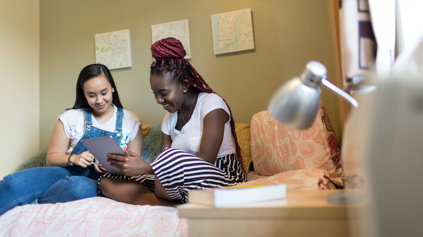 Students sitting on a bed, looking through a book in University accommodation