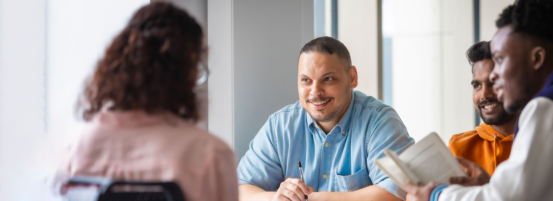 Students sitting around a table, with open books, talking and smiling