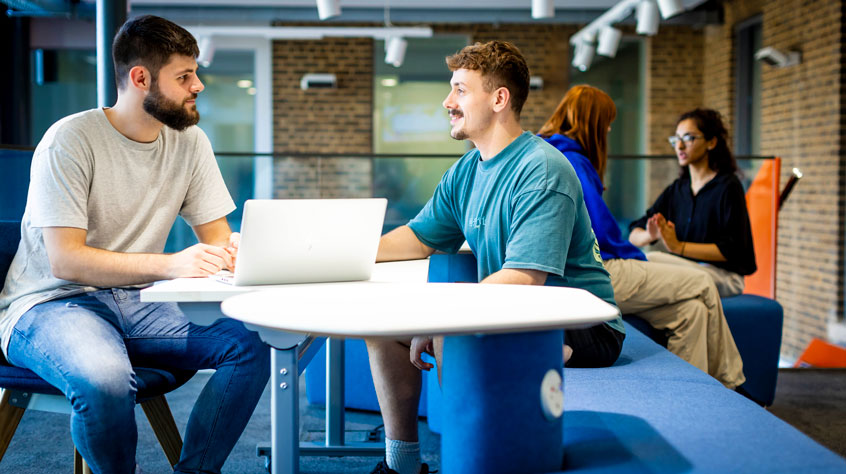 Students sitting at a table, talking over a laptop
