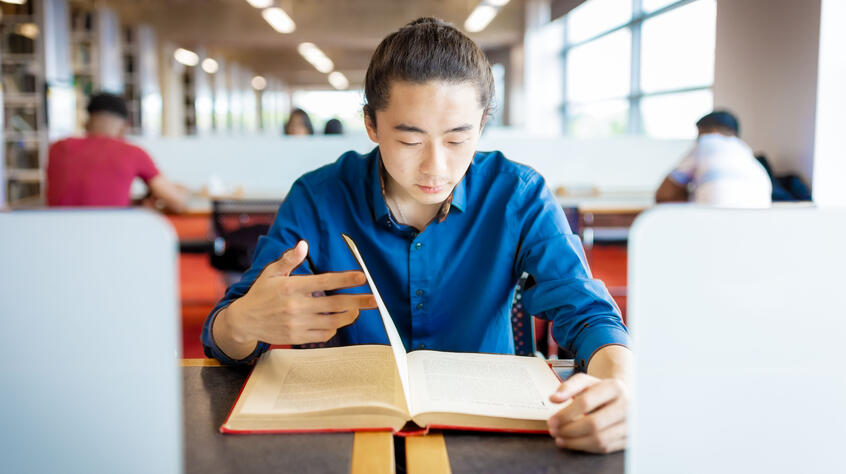 Student reading a book in a communal workspace. 
