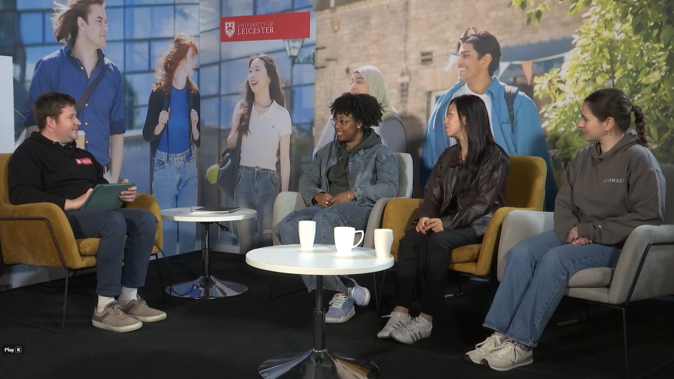 Three students talking to a host on a panel, sat in yellow chairs. 