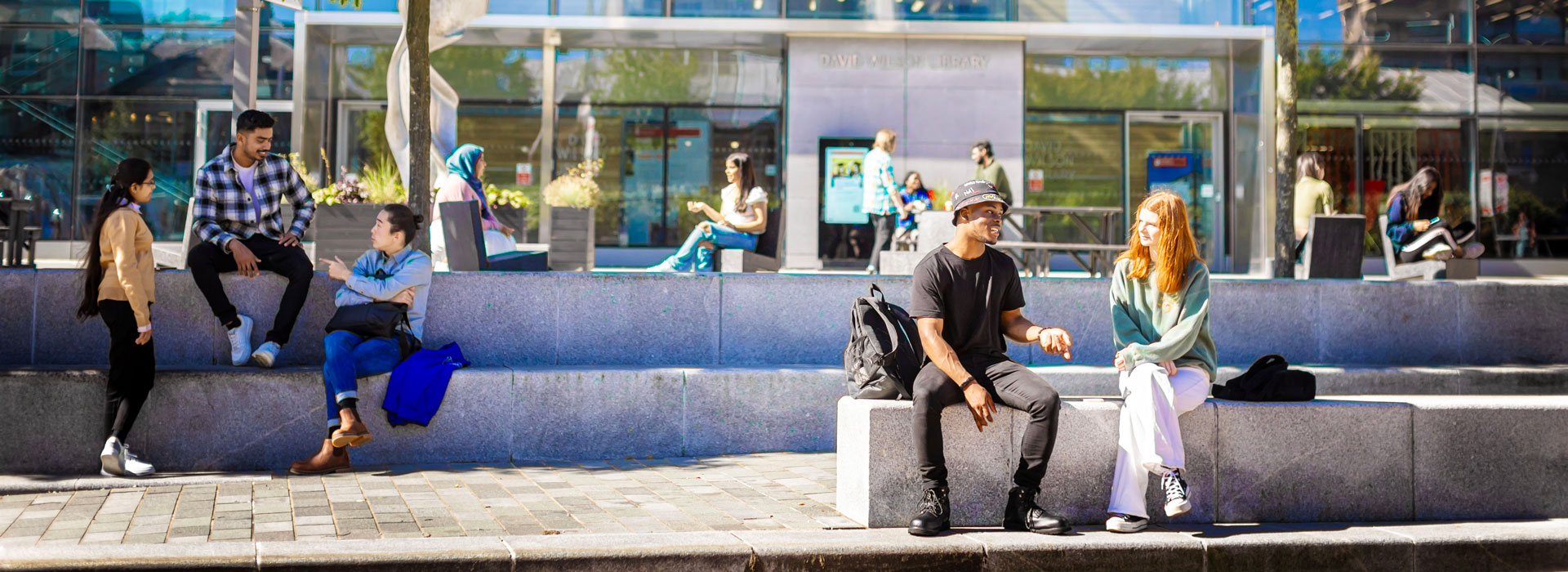 Students sitting on benches outside the David Wilson Library on Leicester campus.