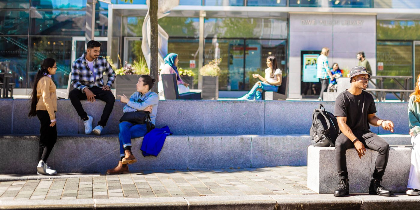 Students sitting on benches outside the David Wilson Library on Leicester campus.