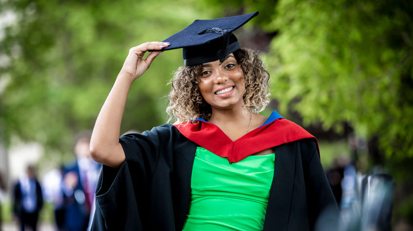 Woman wearing a cap and gown, smiling into the camera, with trees behind her.