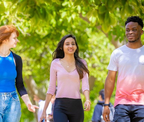 Three students walking though Victoria Park on a sunny day.