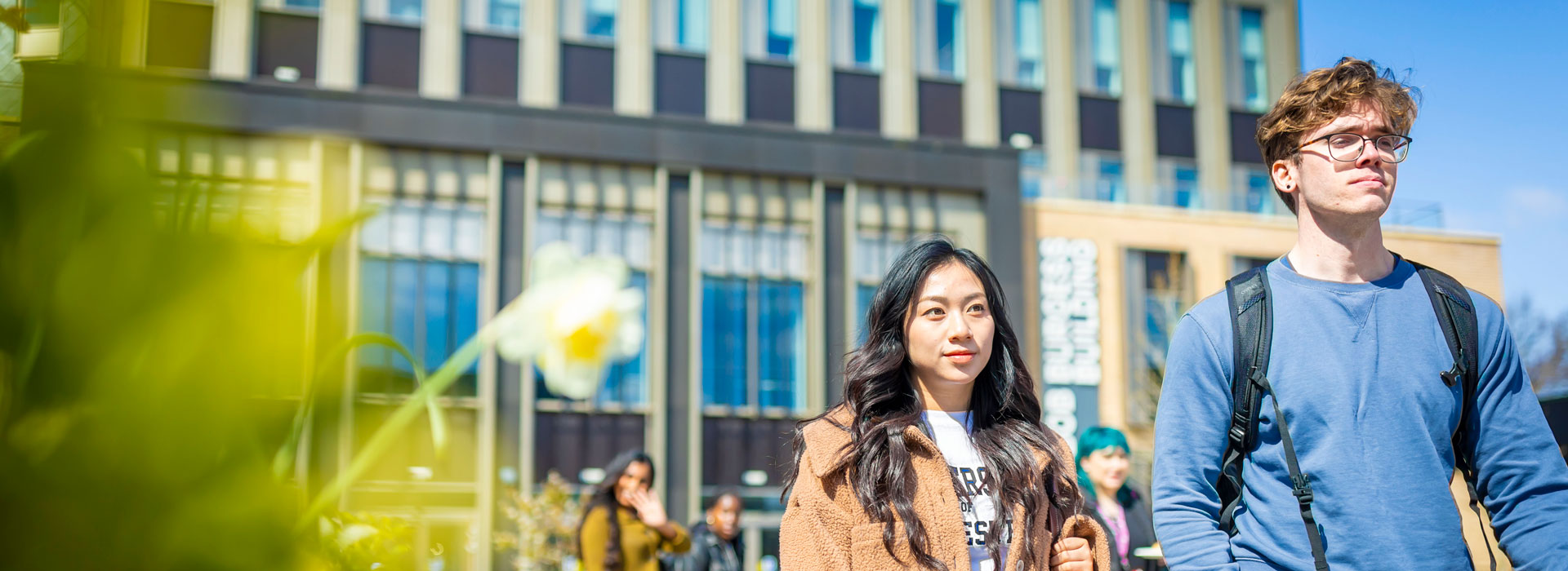 A man and a woman walking outside a large building with blue skies in the background.