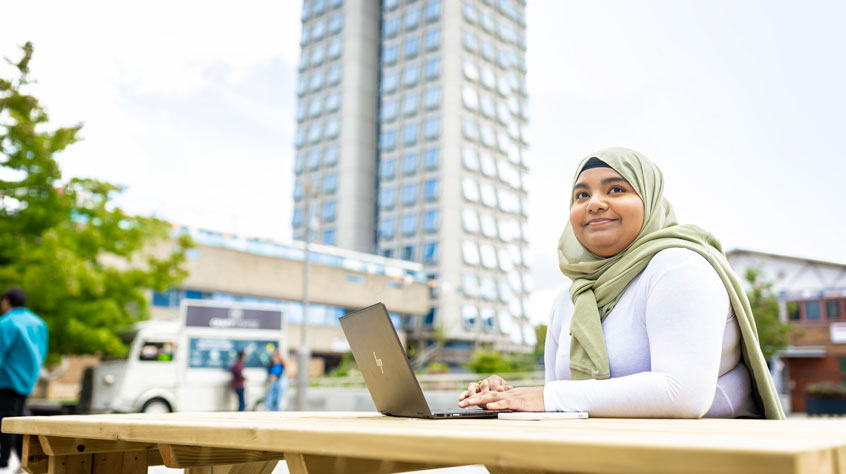 Student sitting on a bench working on a laptop