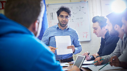 Men standing in front of a teaching desk and holding a piece of paper