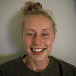 Woman with blonde hair tied in a bun, smiling into the camera