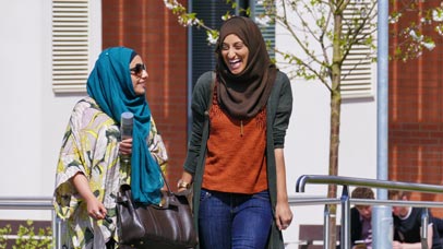 Two students laughing outside the George Davies Centre on Leicester campus