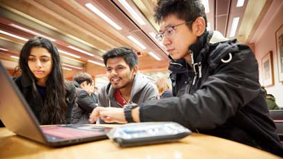 Three students in the library, gathered around a laptop