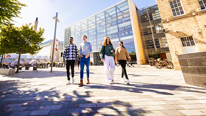 Four students walking through the University of Leicester campus on a sunny day