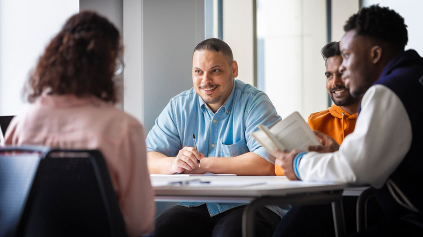 Students sitting around a table talking with open books.