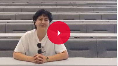 Student sitting in an empty lecture theatre and looking into the camera lens.