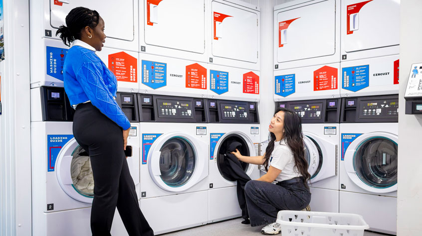 Two people standing next to washing machines in a laundrette.