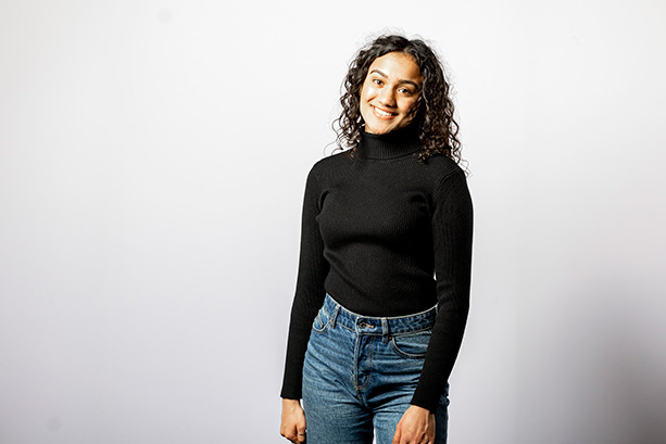 A young woman wearing a black turtleneck sweater and jeans, smiling at the camera.
