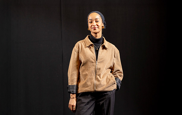 A young woman wearing a jacket and pants, standing confidently.