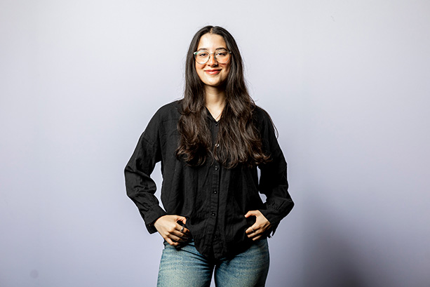 A young woman wearing a black shirt and jeans posing confidently for the camera, smiling.