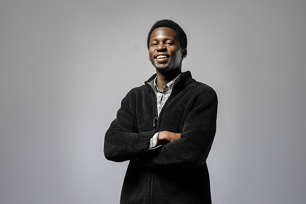 A young man wearing a black sweater, standing confidently.