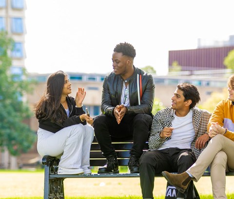 Students sitting on a bench in the park, talking and smiling