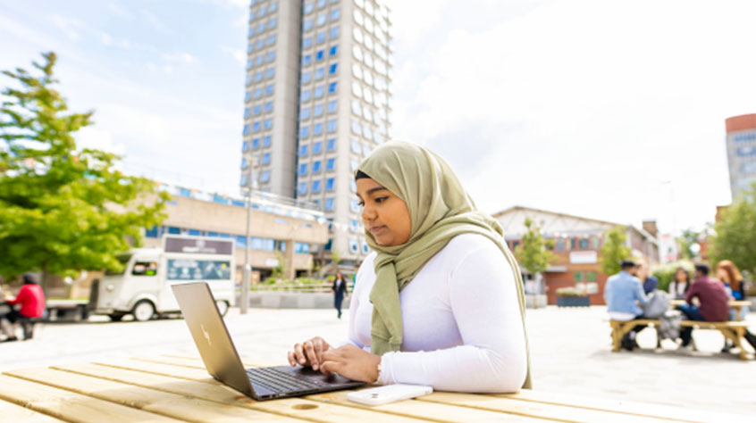 Female student sat outside on her laptop