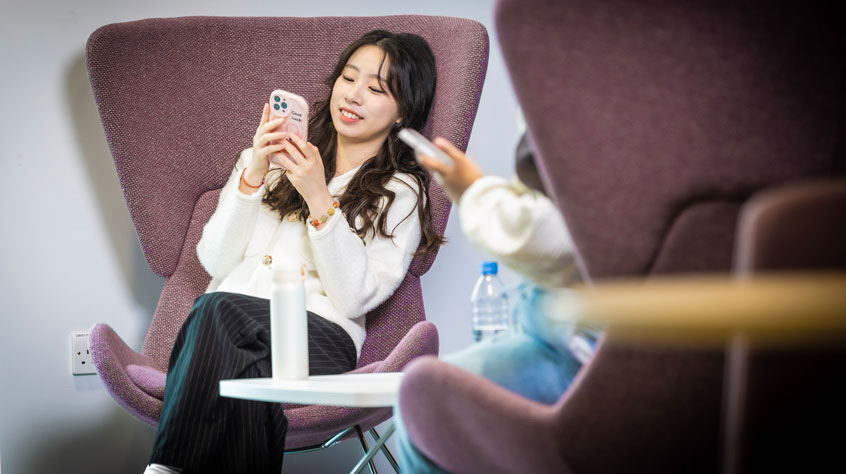 Student looking at her phone whilst on Leicester campus.