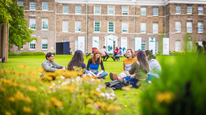 Student sitting on the grass outside the Fielding Johnson Building on Leicester campus.