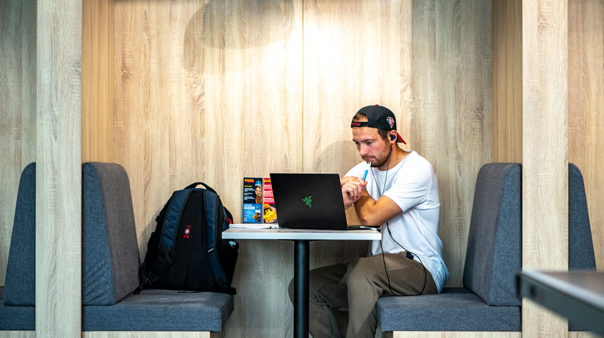 Student working on a laptop in the booth of a cafe.
