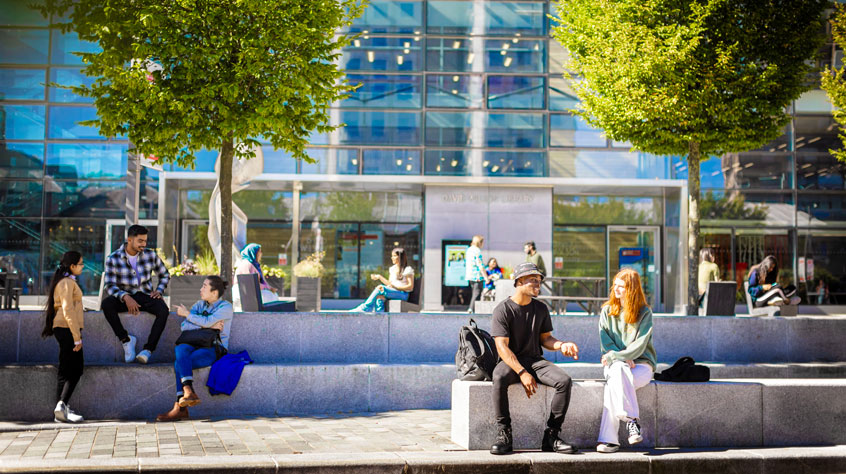 Students sitting round outside the David Wilson Library on a sunny day.